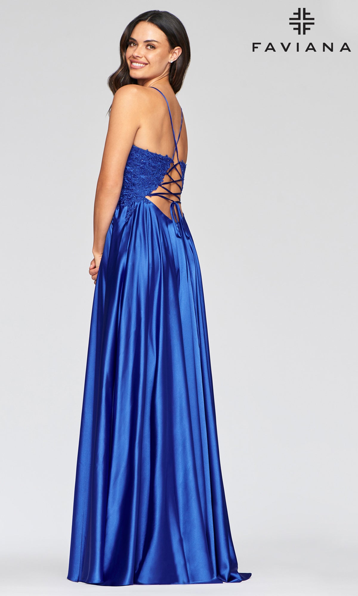 A woman smiles over her shoulder wearing the Faviana Lace-Bodice Long A-Line Prom Dress in royal blue satin, featuring a lace-up back. The Faviana logo appears in the top right corner.